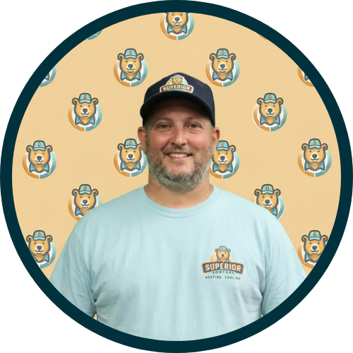 Man wearing a light blue T-shirt with a small logo standing in front of a repeating dog-logo backdrop, circular frame around the image.