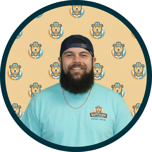 Smiling man with a full beard and a backwards cap, wearing a teal shirt with a brand logo, against a bear-logo patterned backdrop.