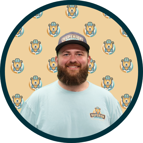 Bearded man in a light blue shirt with a Superior logo on his cap and chest, posed against a beige background with repeating bear logos.