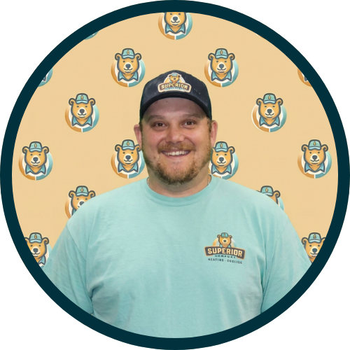 Smiling man in a teal shirt and cap, posing in front of a backdrop covered with bear logos for Superior Heating & Cooling.