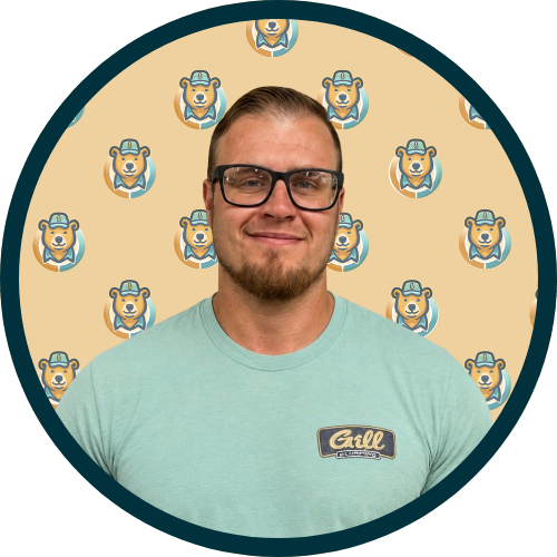 Smiling man with glasses wearing a light teal shirt with a Grill logo, against a beige bear-patterned backdrop.