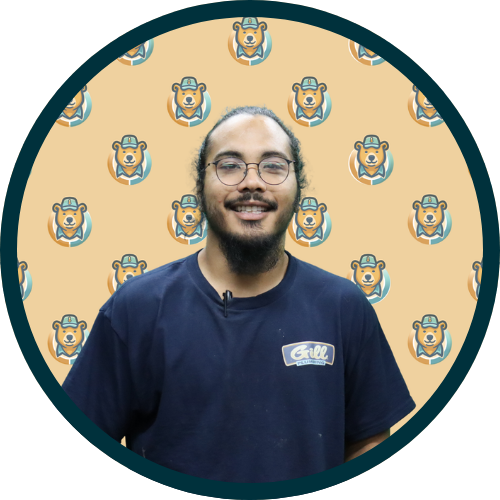 Portrait of a man with glasses and a beard, wearing a navy shirt, standing before a tan background with repeating bear logos.