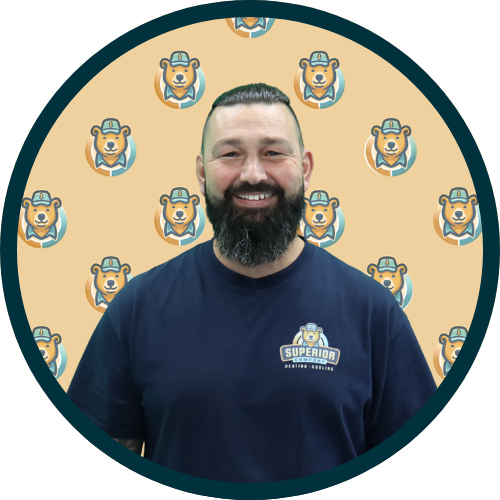 Smiling man with a beard wearing a navy shirt with a logo, standing before a tan background covered in bear mascots.